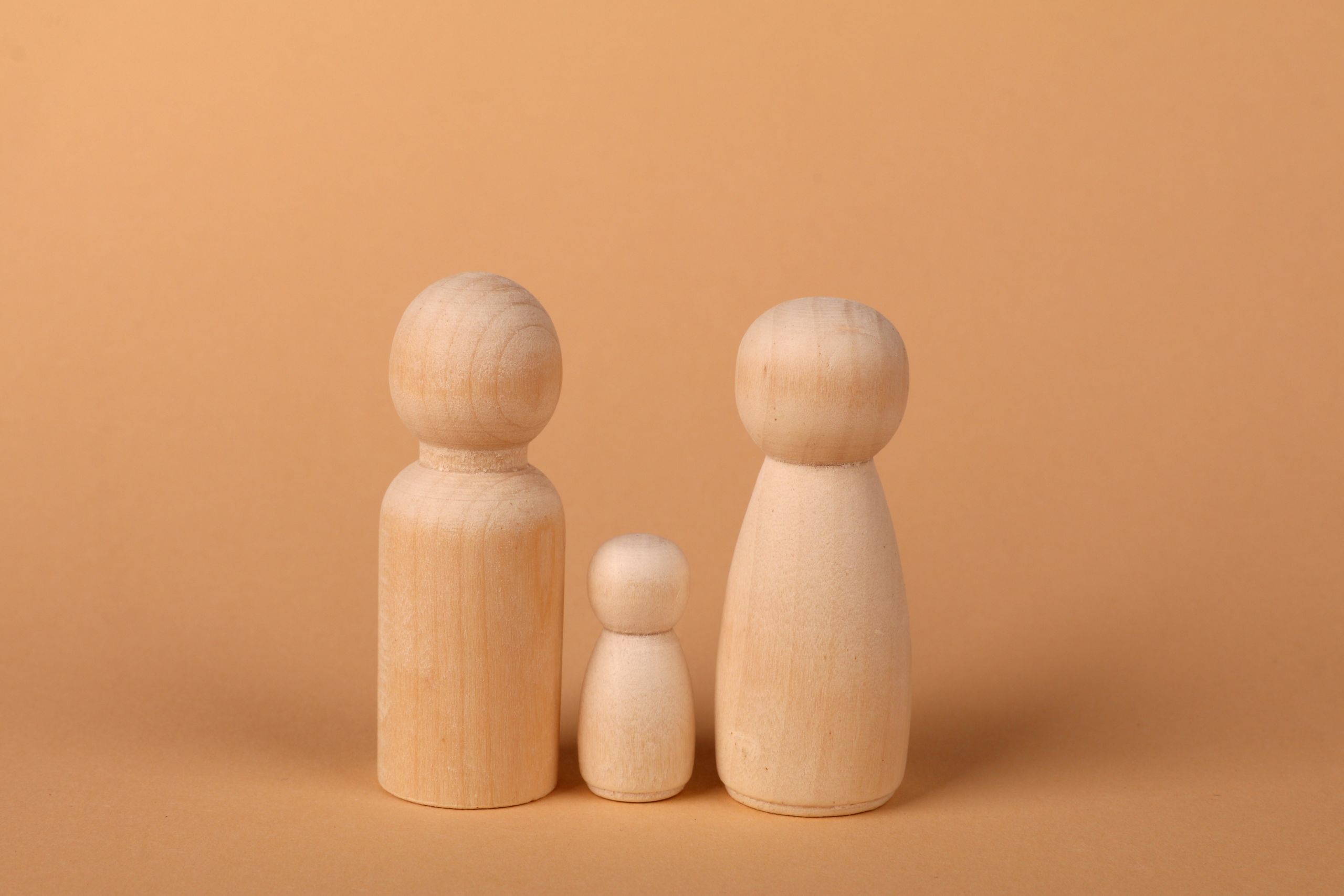 Three wooden figurines representing a family set against a warm brown backdrop.